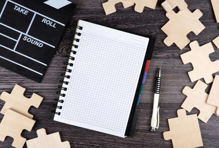 notepad with cinematic clapper, pen and puzzle pieces on a table top viewの写真素材