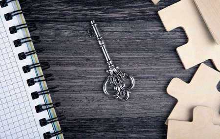 silver key with a notepad and puzzle pieces on a table top viewの写真素材