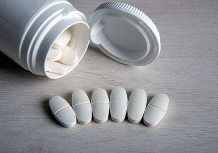 open jar with white pills in a row on a wooden table close upの写真素材