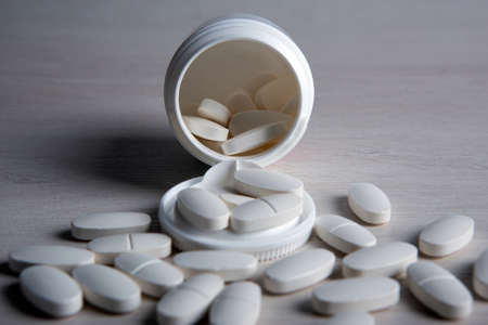 open jar with white pills on a wooden table close upの写真素材