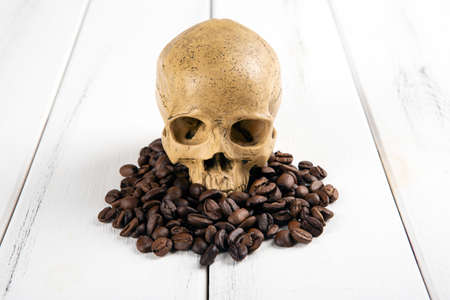 roasted coffee beans with a human skull as a symbol of danger closeupの写真素材