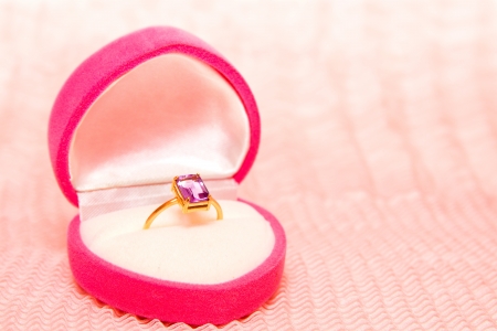 Golden ring with amethyst in pink heart shaped box on pink chiffon textureの写真素材