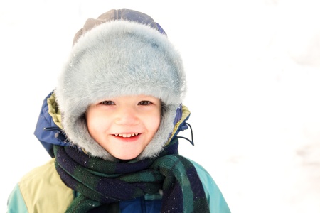 Smiling boy in a warm hat in snow isolated over white (snow) backgroundの写真素材