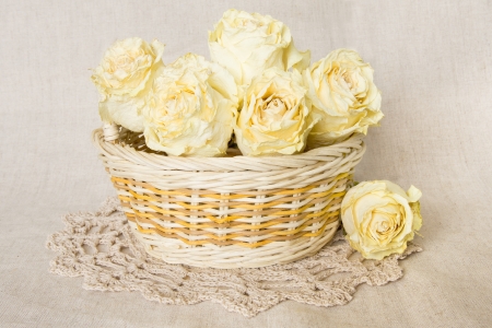 White dried roses in basket with knitted doily over linen background の写真素材
