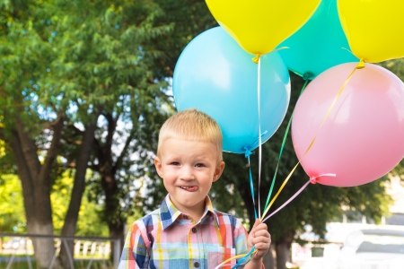 Beautiful happy cute joyful smiling blond child  little boy  with bunch of balloons in hands, close up outdoor portrait, birtday, fun and summer holiday の写真素材