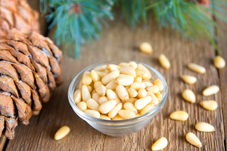 Pine nuts in bowl with cones close up on rustic wooden background, horizontalの写真素材