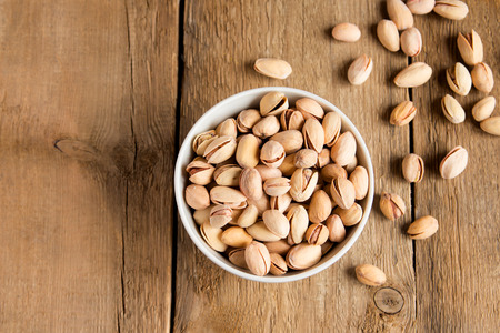 Salty pistachios nuts in bowl on rustic wooden background, close up, horizontal, copy space,...