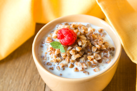 Buckweat porridge with milk, raspberry (berry) and mint on white napkin and wooden table, close up, horizontal. Natural organic vegetarian food (breakfast).の写真素材