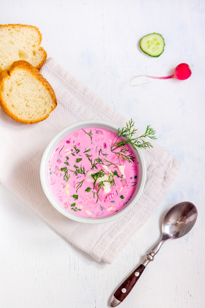 Cold soup with vegetables and herbs in bowl over white wooden table, top viewの写真素材