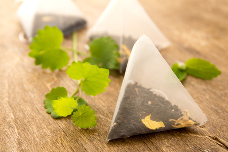 Teabags with fresh green melissa (mint) leaves over rustic wooden background close upの写真素材