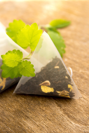 Teabags with fresh green melissa (mint) leaves over rustic wooden background close upの写真素材