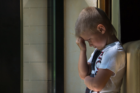 Sad upset waiting boring depressed child (boy) near a window