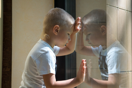 Sad upset waiting boring depressed child (boy) near a window, reflection.の写真素材