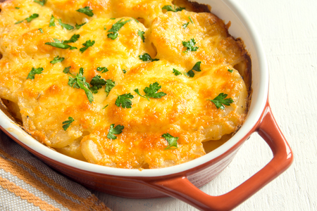 Potato gratin with cream, cheese and parsley in baking dish Potato gratin with cream, cheese and parsley in baking dish
