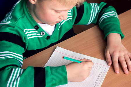 Young caucasian boy doing his elementary school homework while sitting at desk.の写真素材