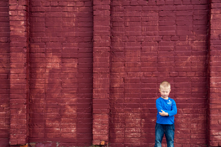 Depressed abused poor little child (boy, kid) sitting near big red brick wallの写真素材