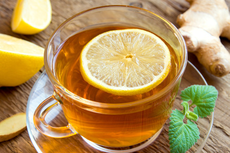 Tea with lemon, ginger, honey and mint leaves in transparent cup over rustic wooden background