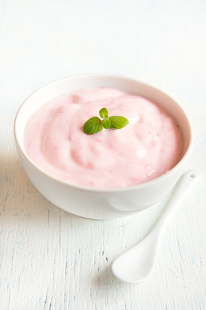 Pink fruit strawberry yogurt in bowl with mint and spoon over white wooden backgroundの写真素材