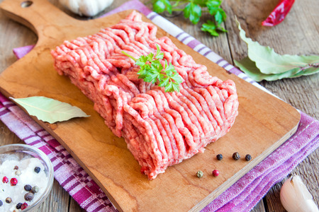 Raw homemade minced meat over wooden cutting board with assorted spices close up