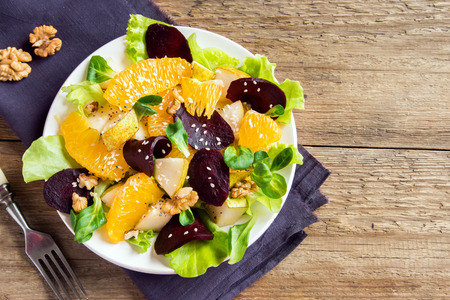 Beetroot and orange salad with greens, pear, nuts and seeds. Healthy vegetarian meal on wooden background with copy space.の写真素材
