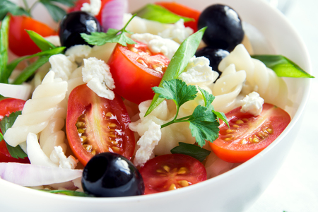 Pasta salad with vegetables, olives and feta over white backgroundの写真素材