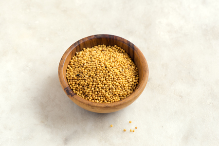 Mustard seeds in wooden bowl over white stone background with copy space - healthy food ingredientの写真素材