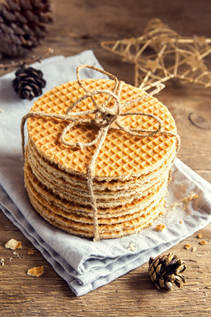 Stack of traditional dutch caramel waffles tied up with jute twine on rustic wooden background with Christmas decor - homemade Christmas pastryの写真素材