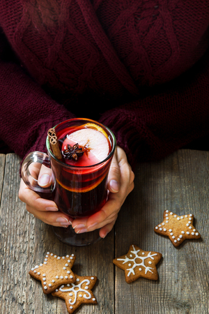 Christmas hot drink - mulled wine in female hands with cinnamon stick, star anise and festive Christmas gingerbread cookies over rustic wooden background, top viewの写真素材
