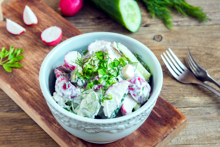 Healthy homemade creamy vegetable salad with greens over rustic wooden background - radish, potato, cucumber creamy salad for healthy spring or summer diet vegetarian lunchの写真素材