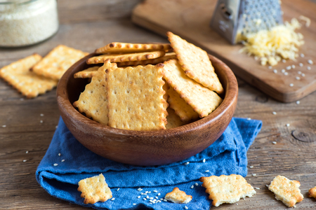 Homemade thin crispy cheesy crackers with sesame seeds in rustic wooden bowl - fresh organic homemade baking cheese crackers snack の写真素材