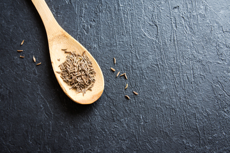 Cumin seeds. Close up image of cumin (zira) seeds on rustic wooden spoon and black background.の写真素材