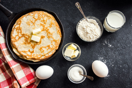 Homemade crepes with butter in cast iron pan and ingredients over rustic black background with copy space - cooking fresh homemade breakfast crepes pancakes foodの写真素材