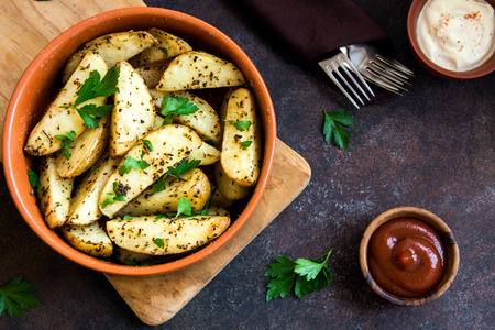 Baked potato wedges with spices and herbs and tomato sauce close up - homemade organic vegetable vegan vegetarian snack food mealの写真素材