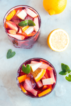 Red wine sangria or punch with fruits, mint and ice in glasses. Homemade refreshing fruit sangria over rustic white table, copy spaceの写真素材