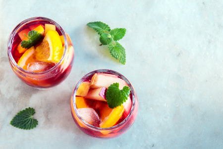 Red wine sangria or punch with fruits and ice in glasses and pincher. Homemade refreshing fruit sangria over rustic wooden table, copy spaceの写真素材