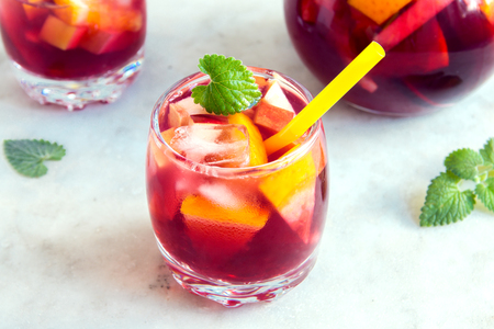 Red wine sangria or punch with fruits and ice in glasses and pincher. Homemade refreshing fruit sangria over rustic wooden table, copy spaceの写真素材
