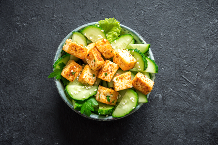 Fried Tofu Salad with Cucumbers and Sesame Seeds. Homemade asian vegetable and tofu salad in ceramic bowl on black stone background. Healthy asian diet vegan vegetarian salad food.の写真素材