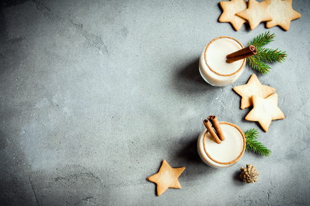 Eggnog with cinnamon and nutmeg for Christmas and winter holidays. Grey concrete background with Christmas Eggnog, gingerbread cookies, pine cones, copy space.の写真素材