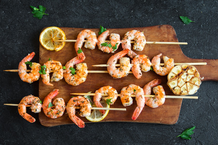Grilled shrimp skewers. Seafood, shelfish. Shrimps Prawns skewers with herbs, garlic and lemon on black stone background, copy space. Shrimps prawns brochette kebab. Barbecue srimps prawns.の写真素材