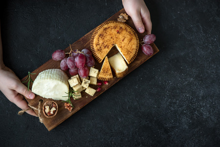 Rustic gourmet cheese platter in hands of cheese maker, top view. Assorted hand made cheese on tray...