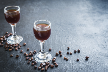Coffee liqueur with coffee beans on rustic black stone background, copy space. Homemade coffee...