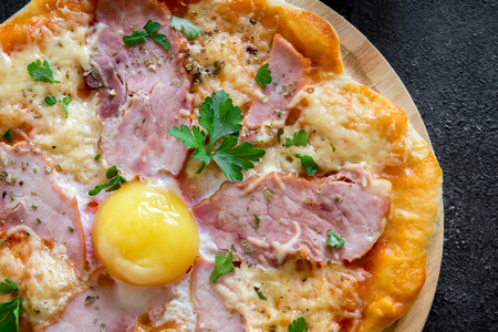 Pizza Carbonara on black stone background. Italian Pizza Carbonara with Bacon, Egg and Cheese close up.の写真素材