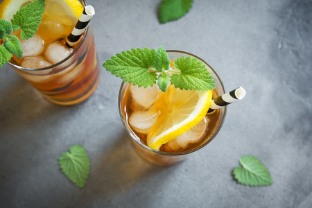 Iced tea with lemon, mint and ice cubes over gray concrete background, copy space. Iced cold summer drink.の写真素材