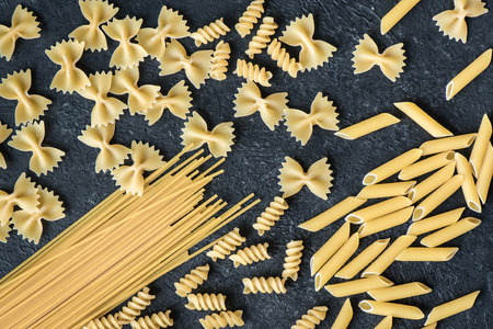 Assorted uncooked raw pasta on black background. Italian pasta: penne, farfalle, spaghetti, fusilli.の写真素材