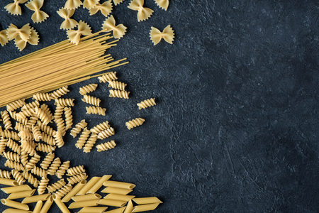 Assorted uncooked raw pasta on black background. Italian pasta: penne, farfalle, spaghetti, fusilli.の写真素材