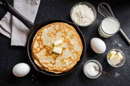Homemade crepes with butter in cast iron pan and ingredients over rustic black background with copy space - cooking fresh homemade breakfast crepes pancakes foodの写真素材