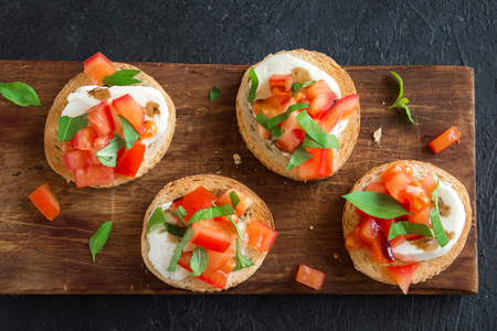 Italian bruschetta with chopped tomatoes, basil, mozzarella cheese and balsamic vinegar. Fresh homemade caprese bruschetta or crostini and ingredients on black background.の写真素材