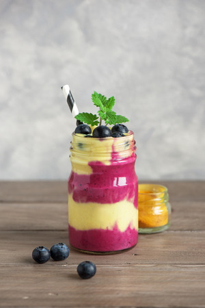 Blueberry and turmeric smoothie for healthy breakfast. Colorful layered smoothie with berries on dark concrete background, copy space.の写真素材