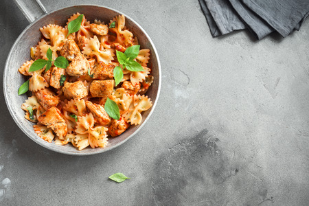 Farfalle pasta in tomato sauce with chicken,  basil in pan. Chicken italian bow tie pasta over concrete background with copy space, homemade italian food.の写真素材