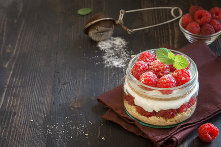 Raspberry cheesecake dessert in glass jar with fresh raspberries and cream cheese on wooden...